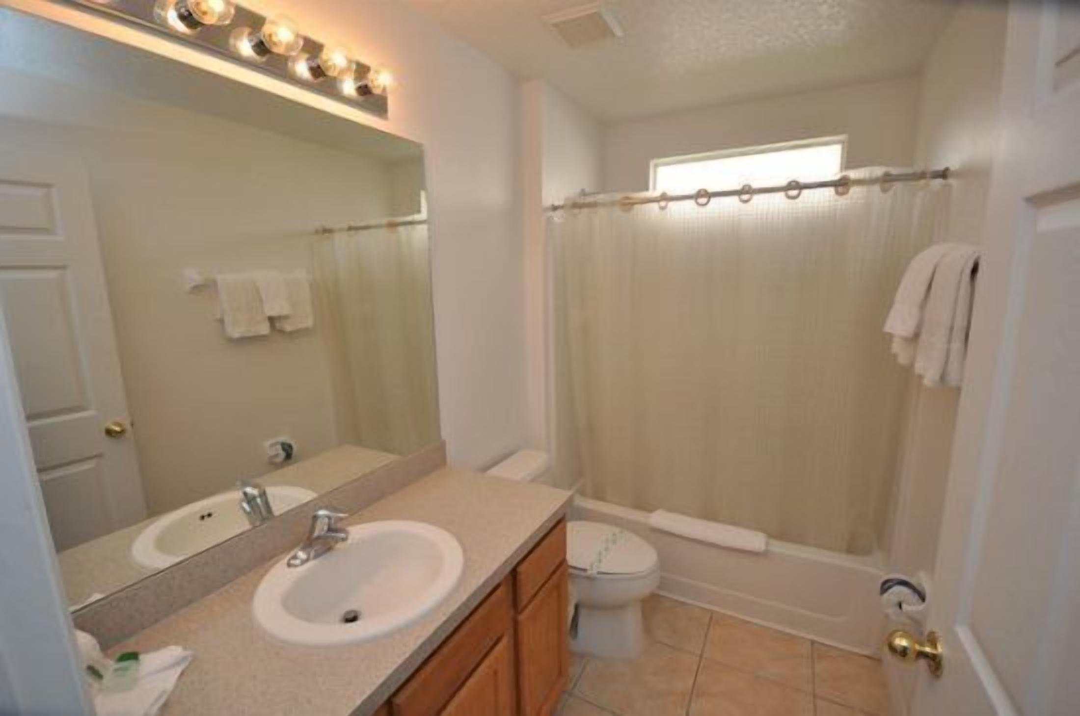 A bathroom with a double sink vanity, a toilet, a shower curtain, and a window.