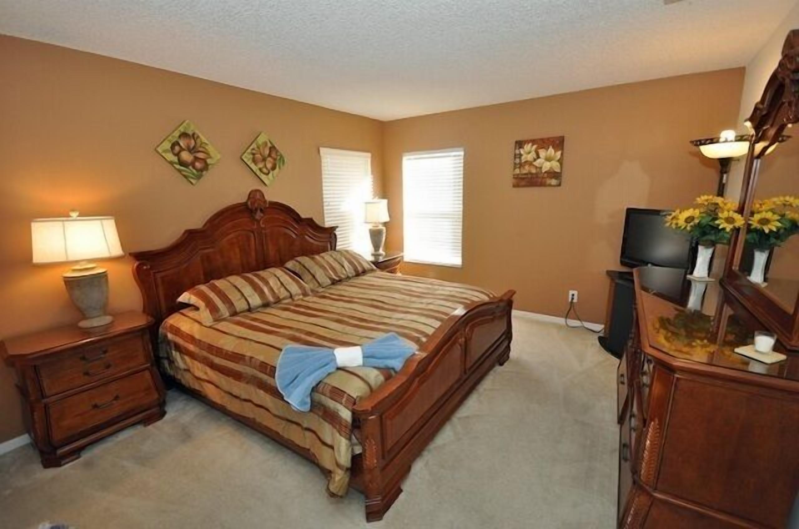 A bedroom with a wooden bed, two bedside tables with lamps, a TV, and a dresser.