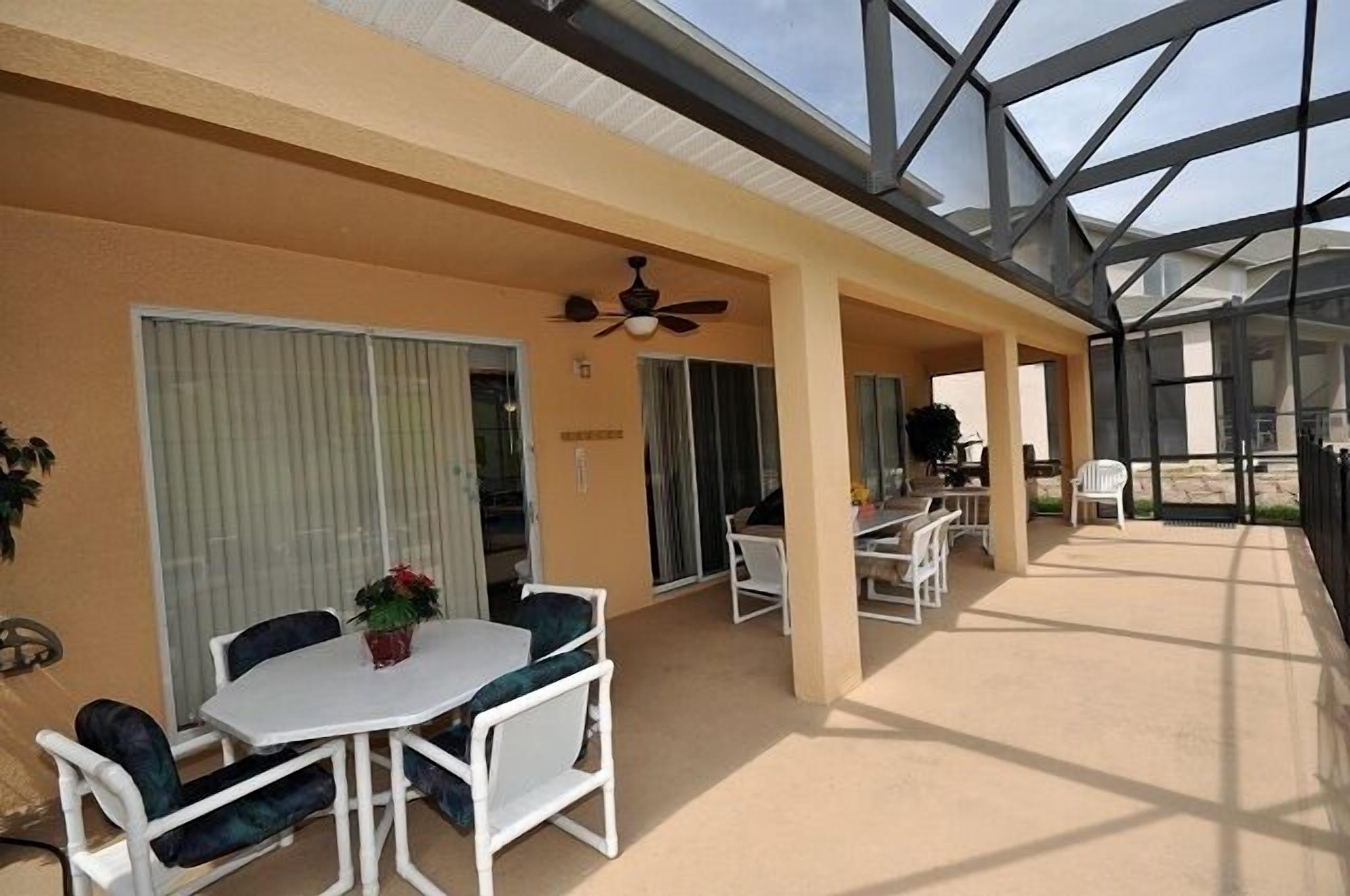 A covered outdoor area with a table and chairs, a ceiling fan, and a glass enclosure.