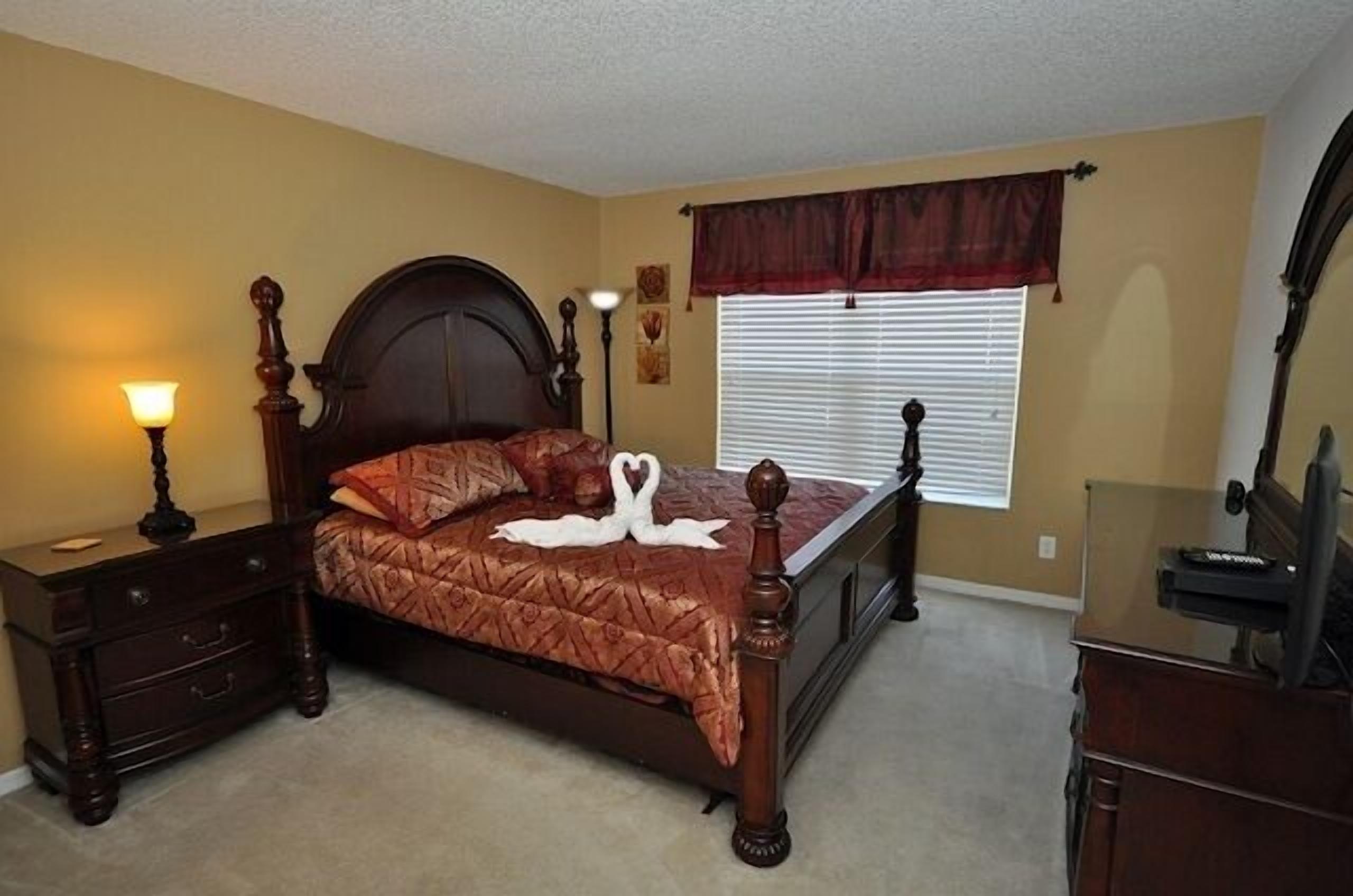 Une chambre à coucher avec un lit, une table de chevet, une lampe et une fenêtre avec des stores.
