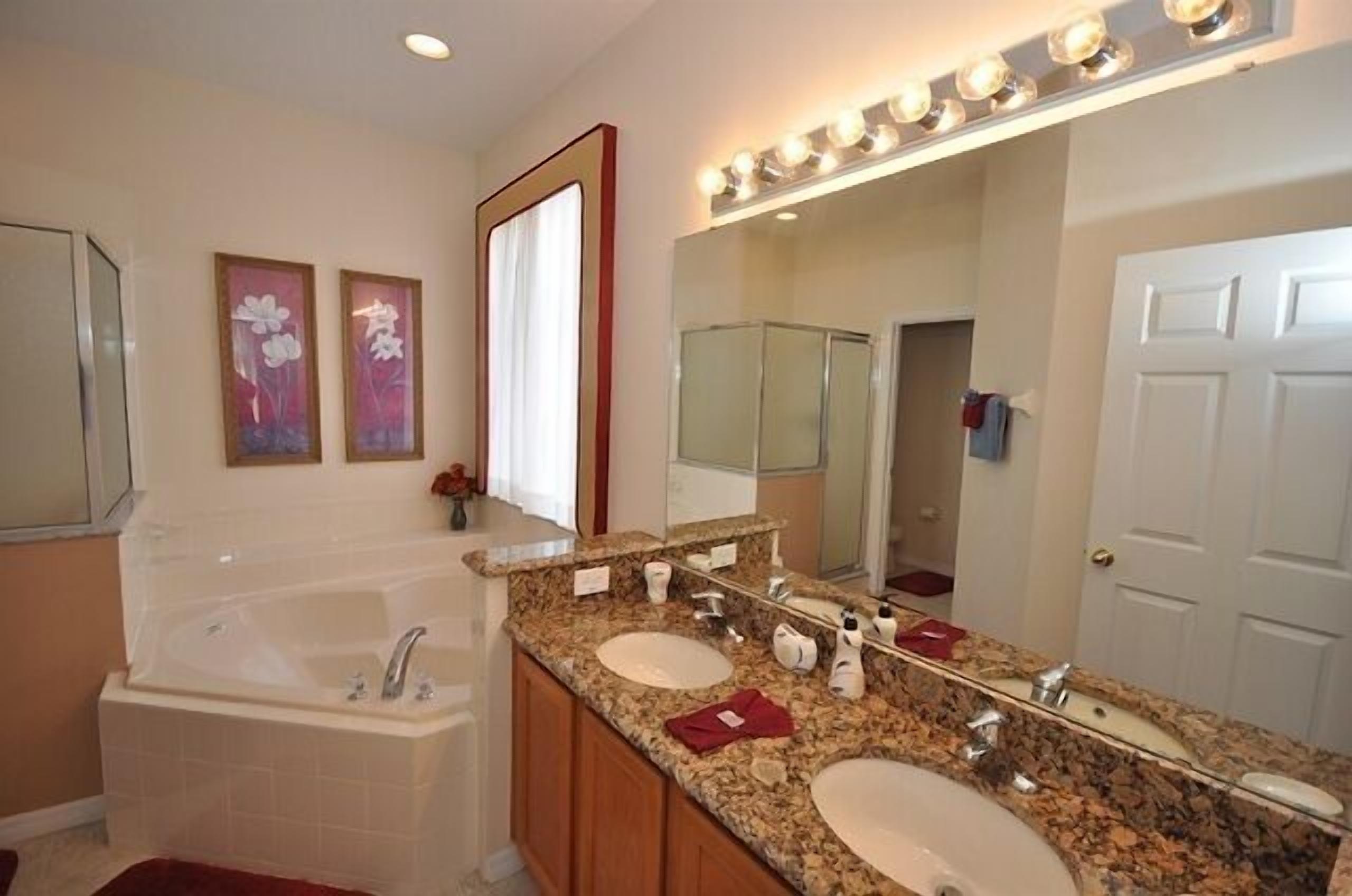 A bathroom with a large mirror, two sinks, a bathtub, and a vanity with a vanity mirror.