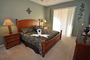 Een slaapkamer met een houten bed, twee nachtkastjes met lampen, een decoratief wandobject en een raam met gordijnen.