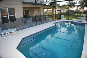 Une piscine dotée d’une enceinte en verre, entourée de chaises longues et d’un espace patio couvert.
