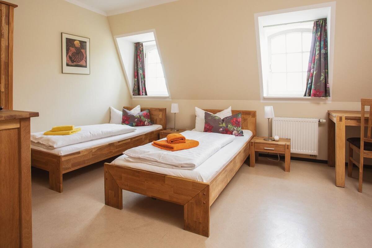 A room with two wooden beds, a small table, a chair, and a window with curtains.