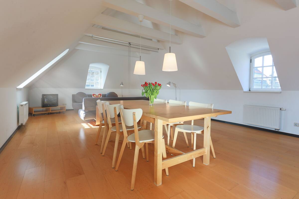 A spacious room with a wooden dining table and chairs, a television, and a window with a view.