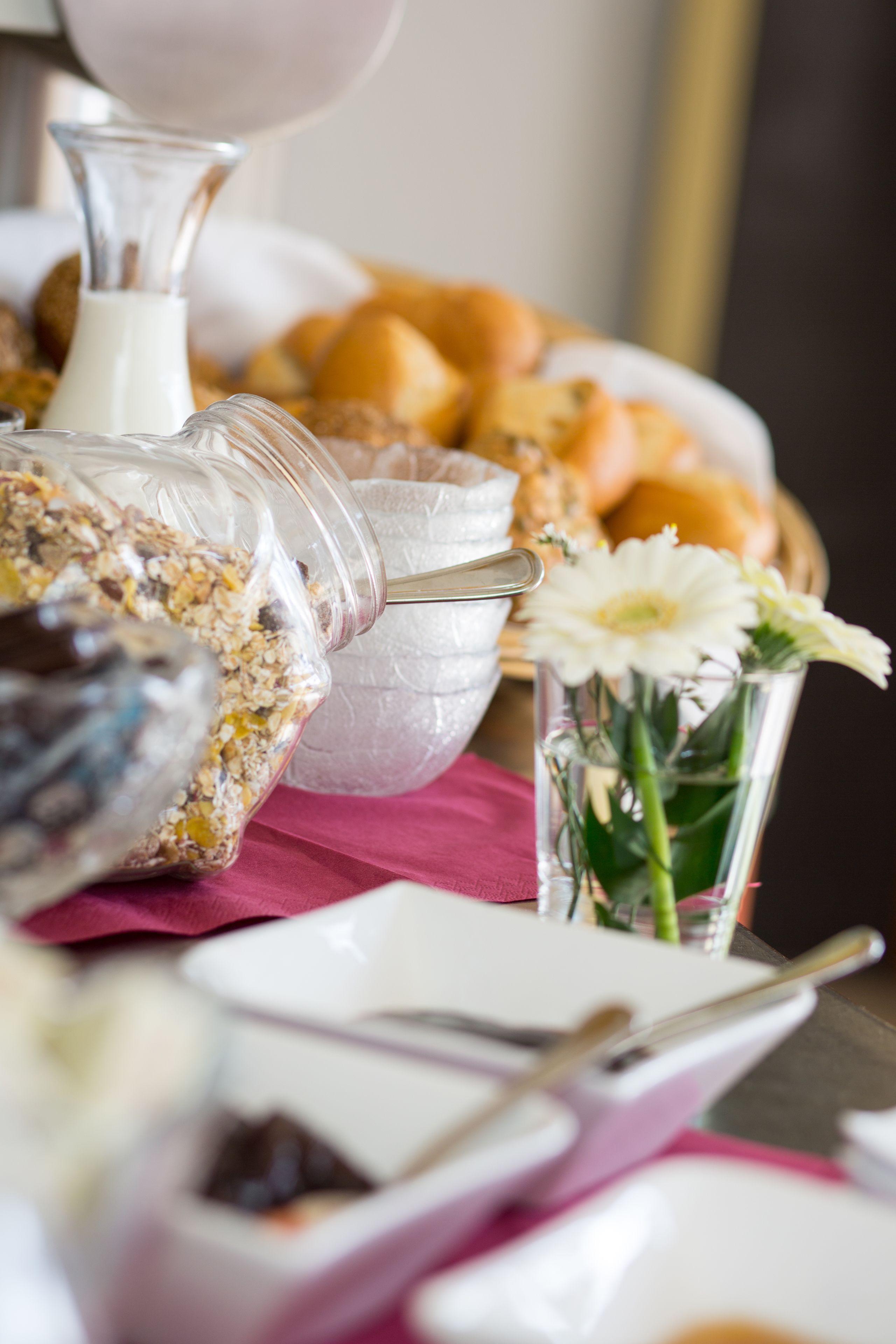 A breakfast buffet with various food items and a glass vase with flowers.