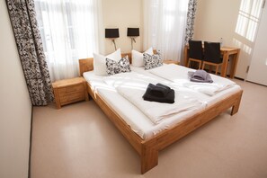 A neatly made double bed with white linens and decorative pillows, a wooden nightstand, a small table with chairs, and two wall-mounted lamps.