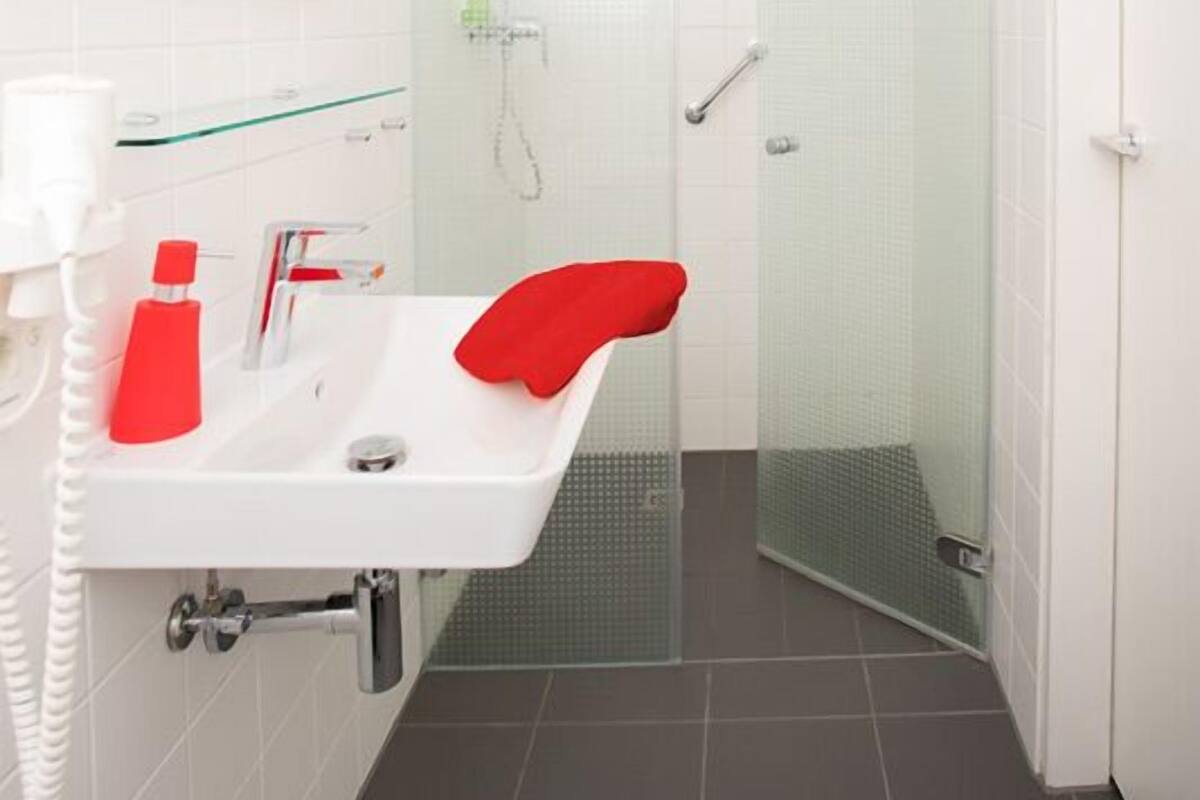 A modern bathroom with a white sink, red towel, and a glass shower enclosure.