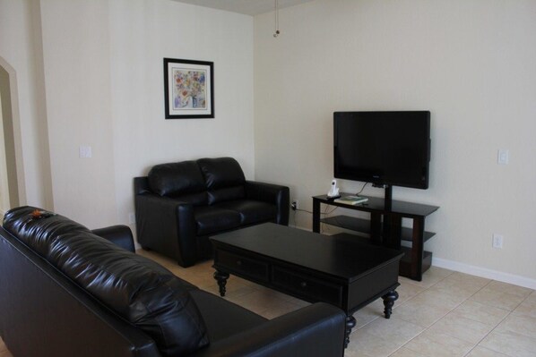 A living room with a black leather sofa, a matching armchair, a coffee table, and a TV on a stand.