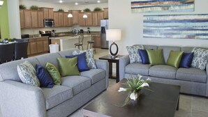 A modern living room with two grey sofas, a coffee table, and a kitchen in the background. - Ov2668 - Paradise Palms - 6 Bed 5 Baths Villa (Kissimmee)