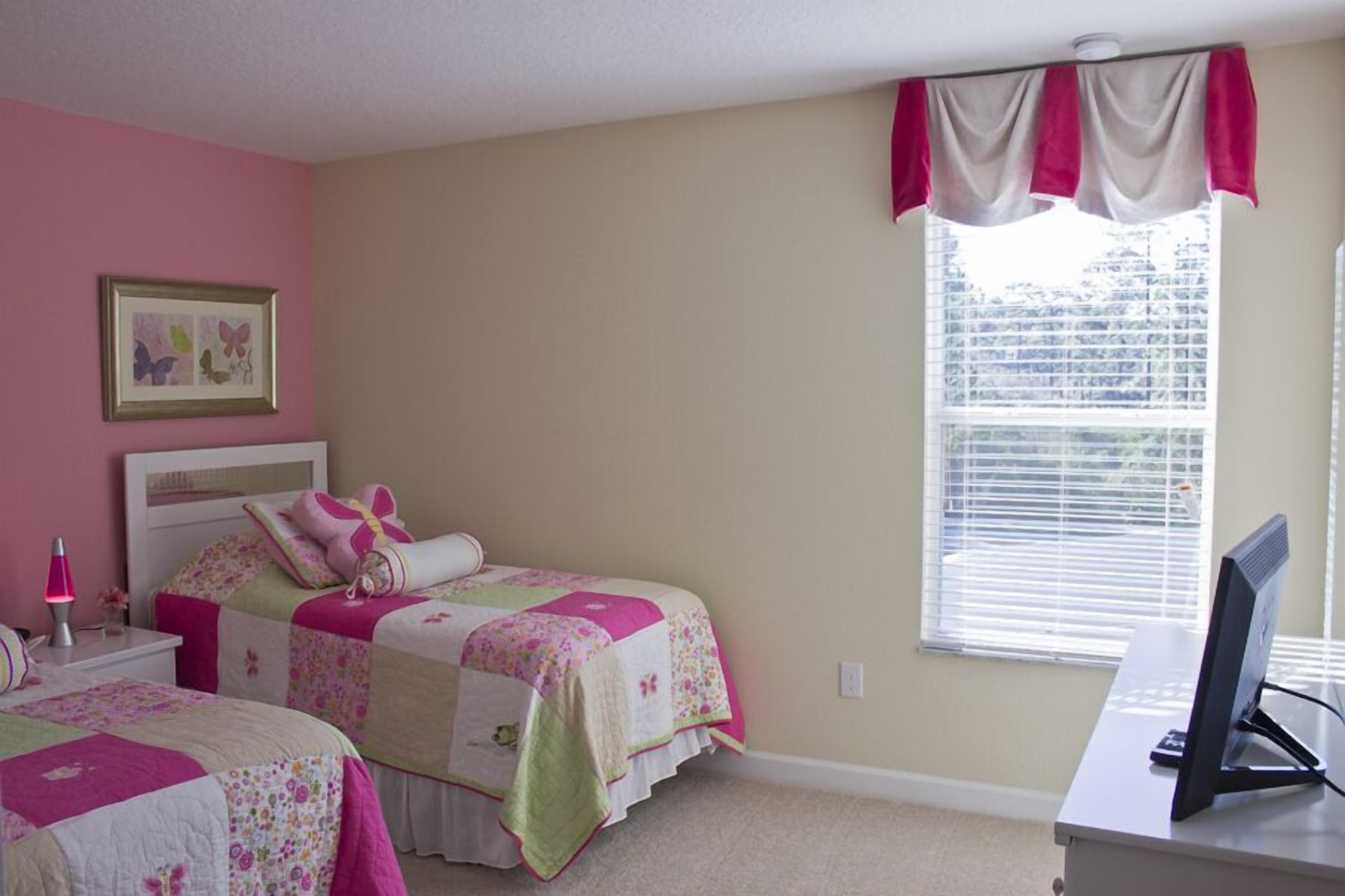 A bedroom with two beds, a desk, a computer, and a window with blinds.
