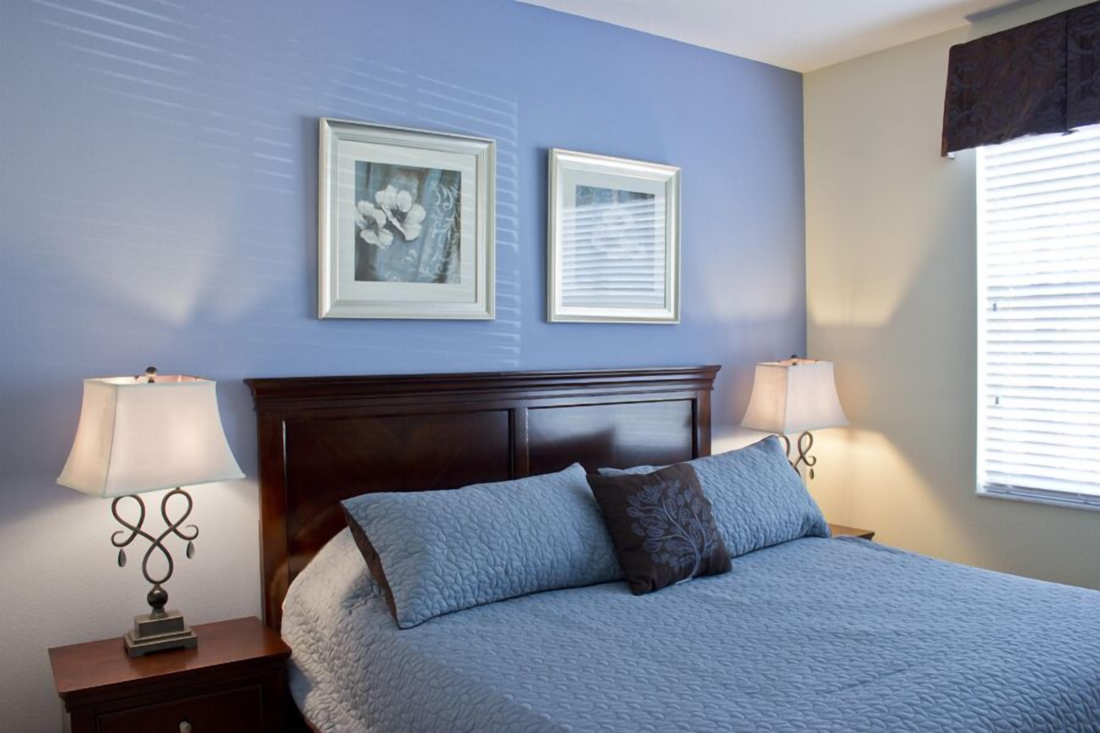 Een slaapkamer met een groot bed, twee bedlampen en twee ingelijste foto's aan de muur.