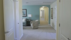 A hallway with a light-colored carpet, a grey sofa, a patterned armchair, and a framed picture on the wall. - Ov2668 - Paradise Palms - 6 Bed 5 Baths Villa (Kissimmee)