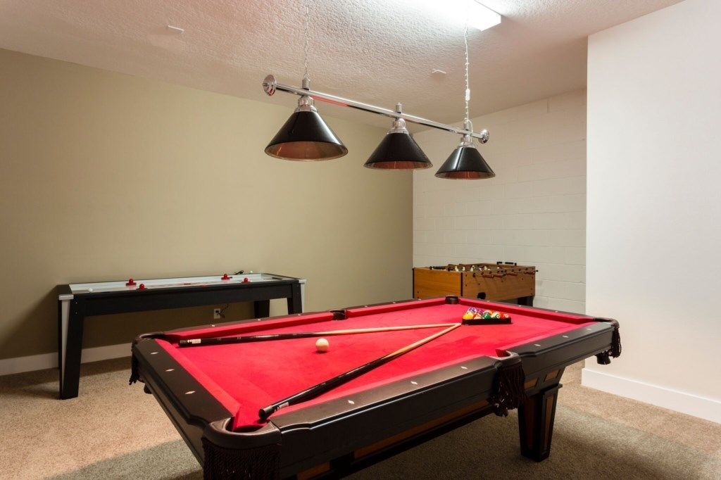 Een pooltafel met een rode viltbekleding, een biljartkeu en drie hanglampen erboven.
