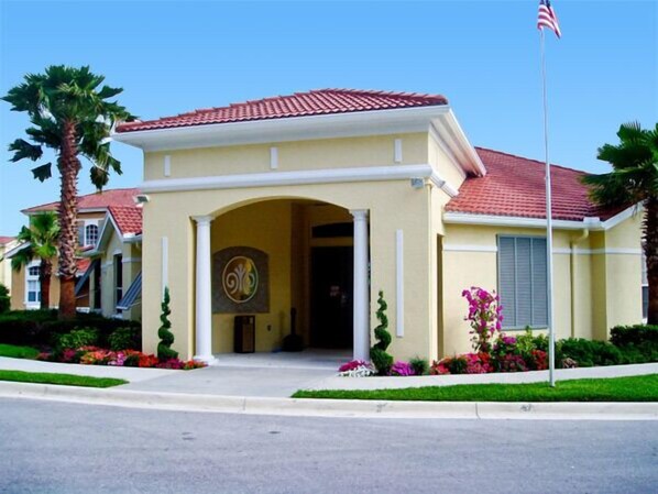 A two-story house with a red-tiled roof, a central entrance with an archway, and a flagpole with an American flag.