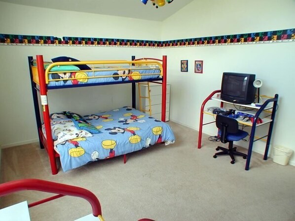Una cama litera infantil con una colcha temática de Mickey Mouse, un escritorio con una computadora y una silla.