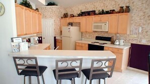 Una cocina con una isla central, armarios de madera, microondas y refrigerador. Hay tres taburetes de bar en la isla.