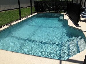 Ein rechteckiger Pool mit klarem, blauem Wasser, umgeben von einer beigefarbenen Liegefläche und einem schwarzen Zaun.