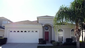 A single-story house with a white garage, a red door, and a small porch with a palm tree. - Ov2562 - Windsor Palms Resort - 4 Bed 3 Baths Townhome (Kissimmee)