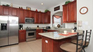 A kitchen with wooden cabinets, stainless steel appliances, granite countertops, and a central island with bar stools. - Ov2542 - Windsor Hills Resort - 6 Bed 4 Baths Villa (Kissimmee)