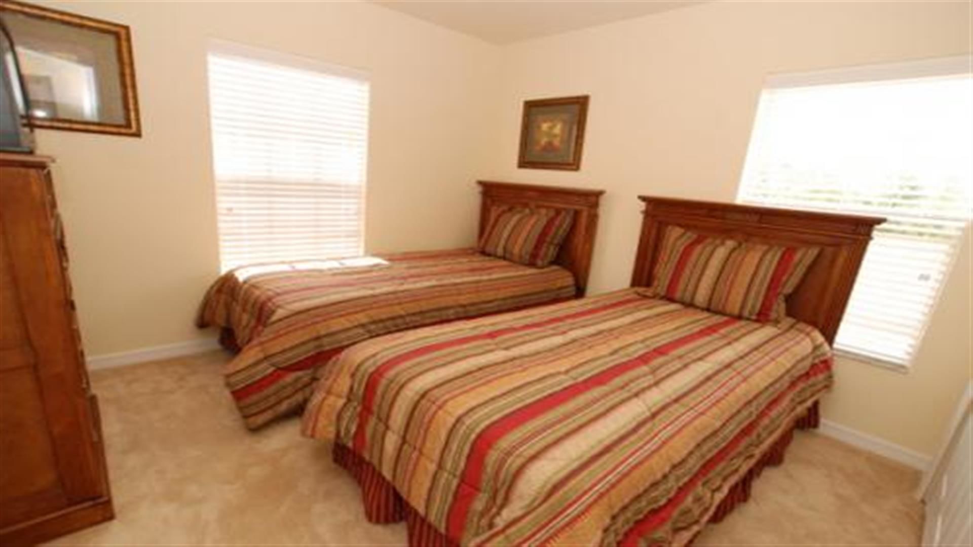 A bedroom with two single beds, a wooden wardrobe, and a framed picture on the wall.
