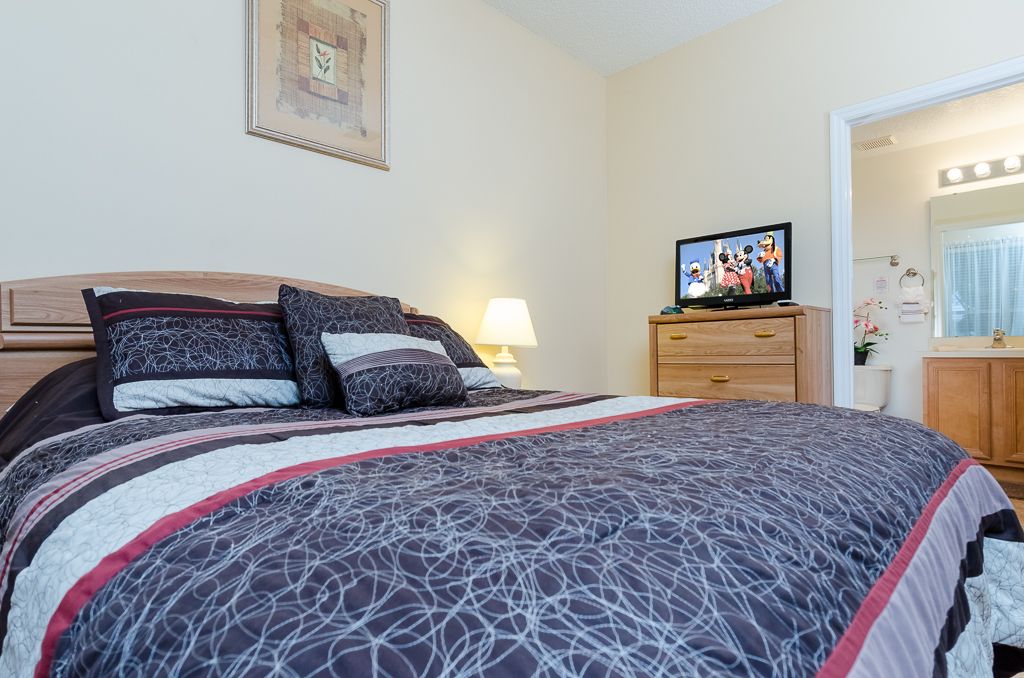 A bedroom with a large bed, a TV on a dresser, and a mirror in the corner.