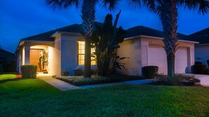 A residential house with a garage, a well-maintained lawn, and palm trees.