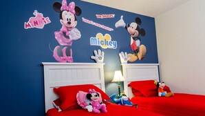 A child's bedroom with Mickey and Minnie Mouse decals on the wall, two beds with red bedding, and plush toys on the beds.