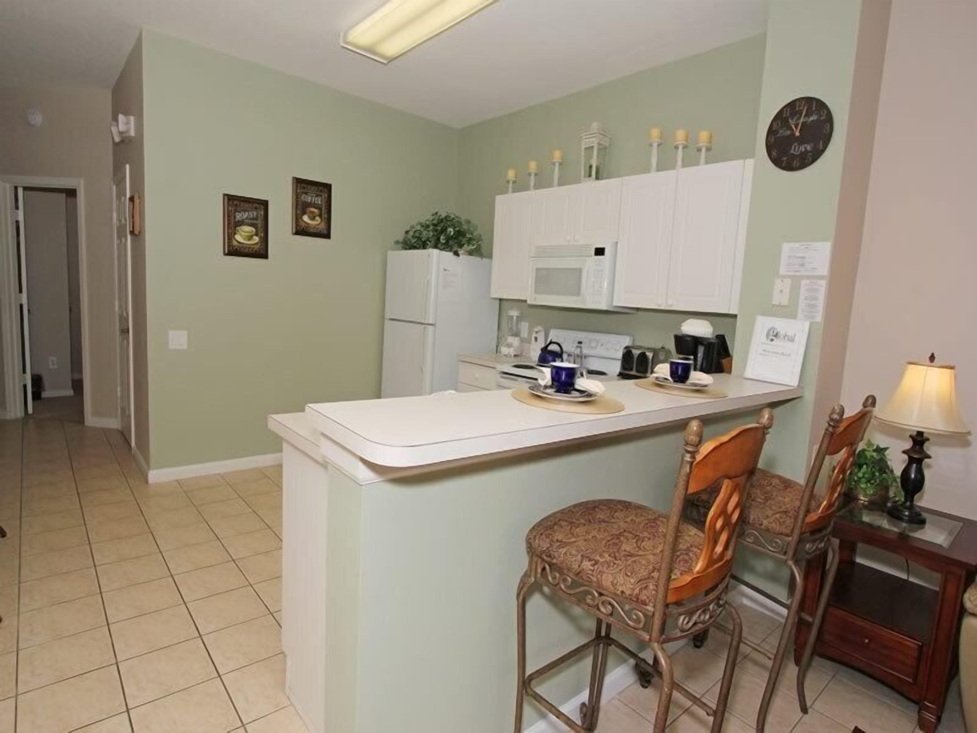 A compact kitchen with a central island, two bar stools, a microwave, and a refrigerator.