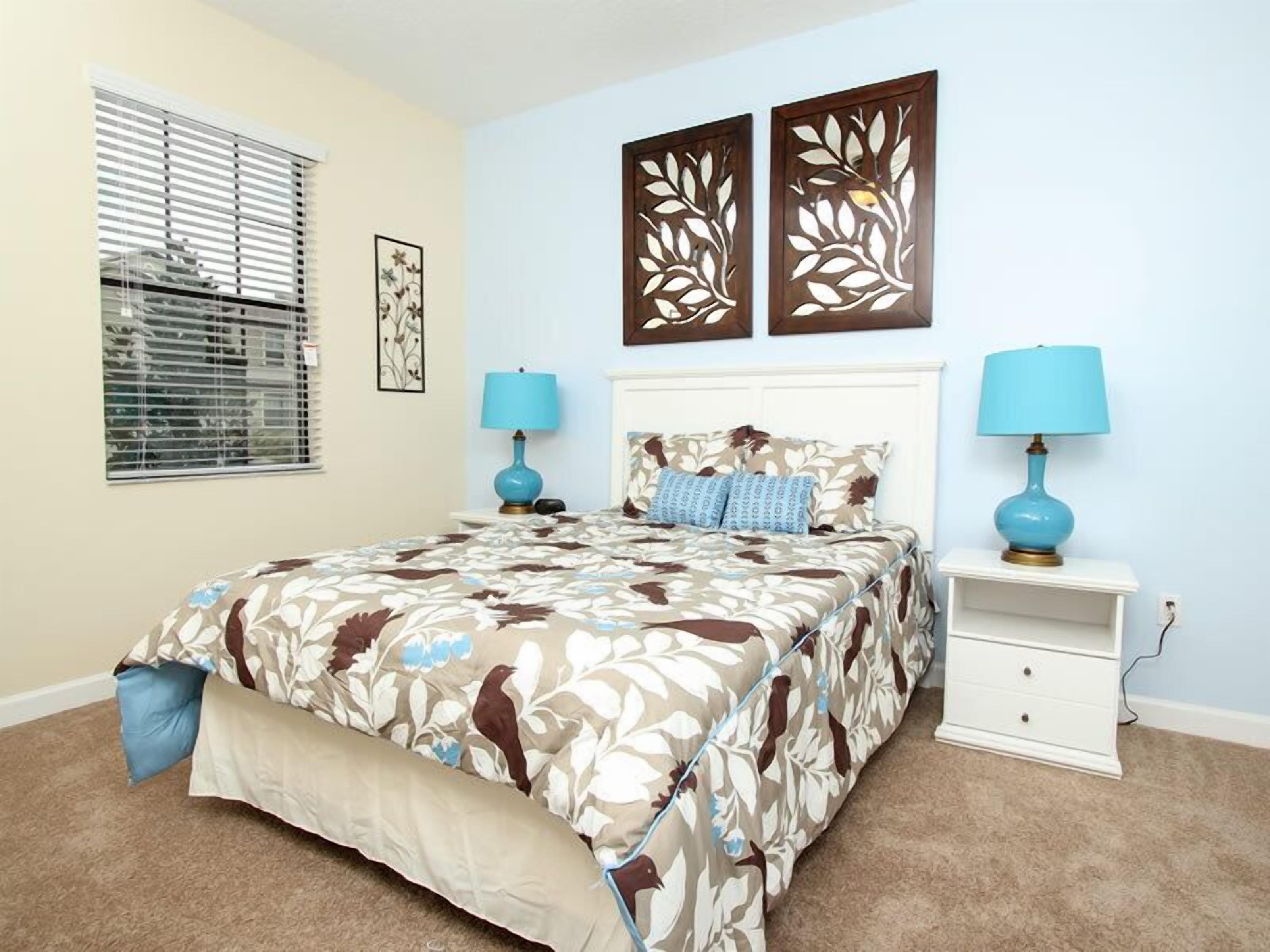 A bedroom with a bed, two nightstands, a window with blinds, and two wall art pieces.