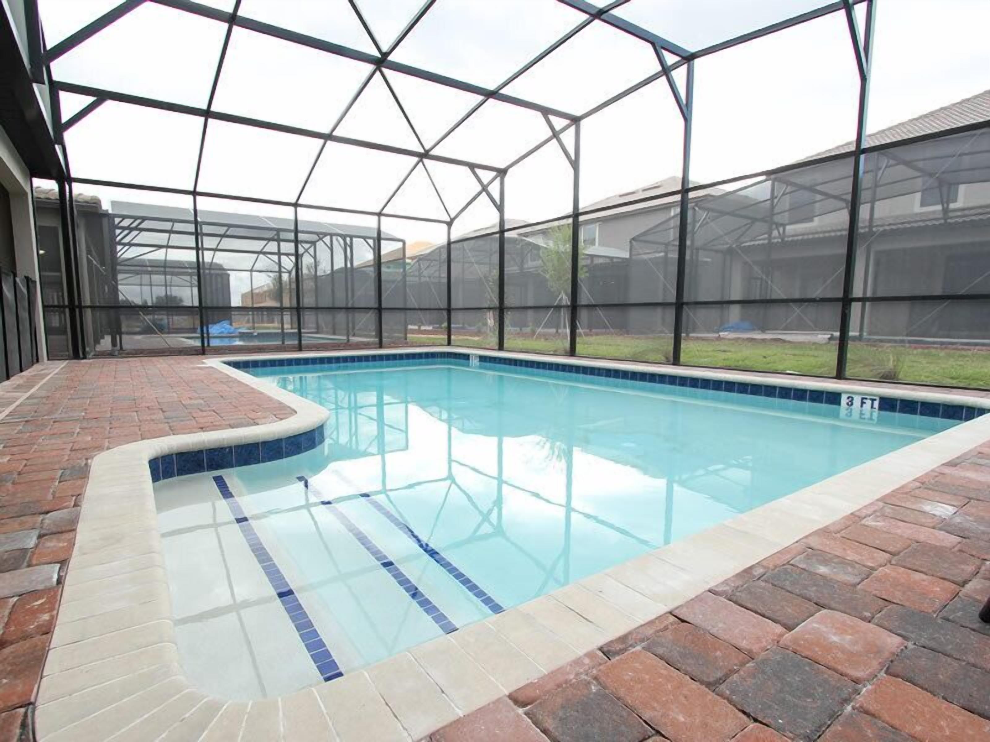 An indoor swimming pool with a glass enclosure, surrounded by brick flooring and a clear blue pool edge.