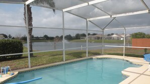 A covered outdoor swimming pool with a view of a lake and houses in the background. - Ov2487 - Hampton Lakes - 5 Bed 3 Baths Villa (Davenport)