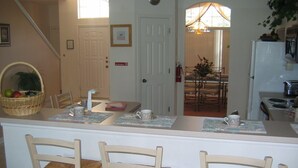 A kitchen with a dining area, including a table with chairs, a refrigerator, and a basket of fruit. - Ov2487 - Hampton Lakes - 5 Bed 3 Baths Villa (Davenport)
