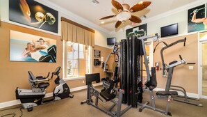 Un gimnasio con diferentes equipos de ejercicio, un ventilador de techo y carteles motivacionales en las paredes.