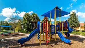 Un parque infantil con toboganes y estructuras para escalar, rodeado de árboles y un cielo despejado.