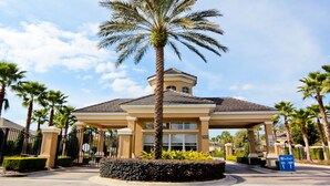 A covered pavilion with a palm tree in front, surrounded by palm trees and a well-maintained hedge.