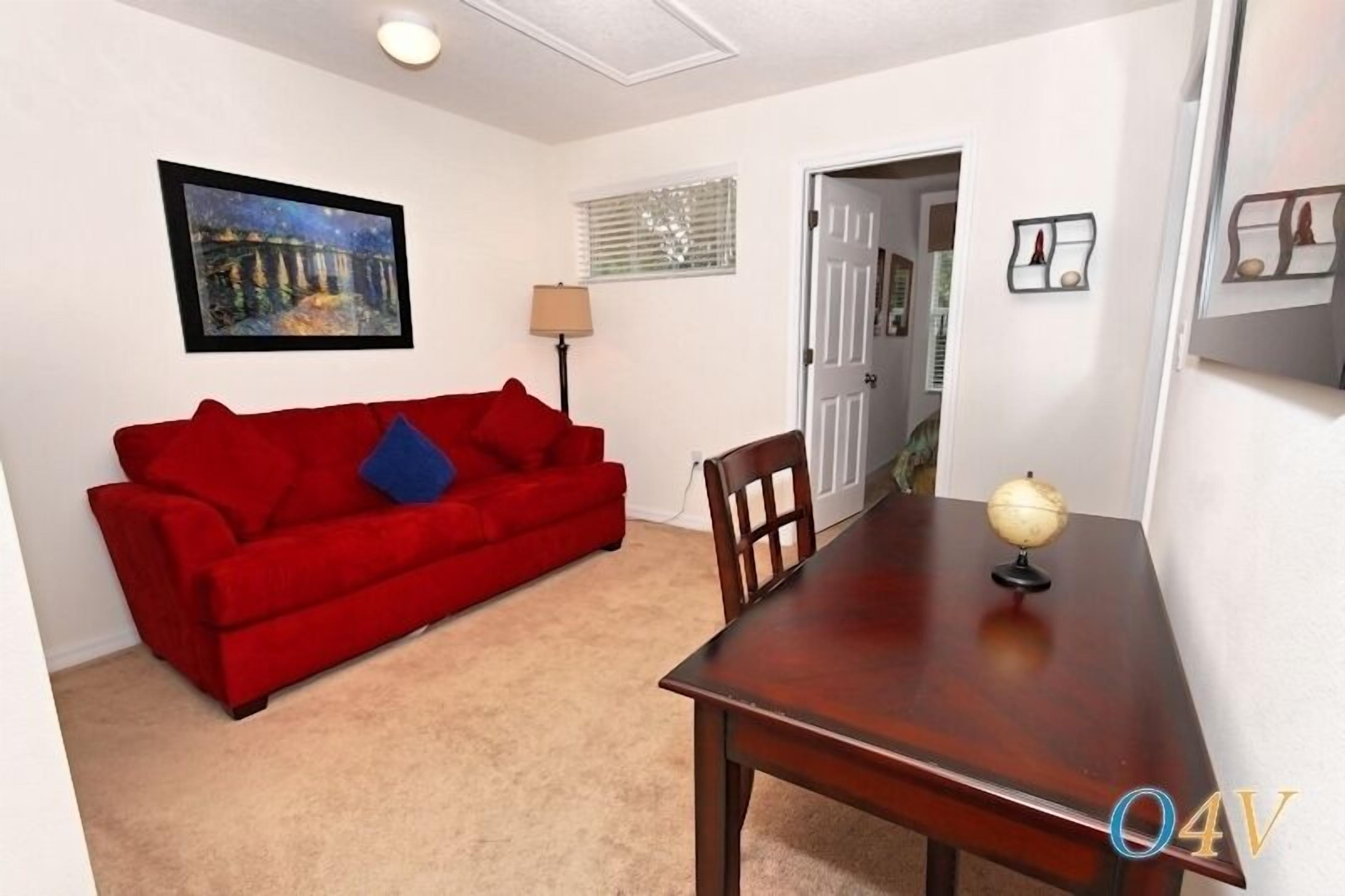 A room with a red sofa, a wooden dining table, a globe, and a painting on the wall.