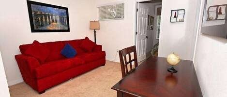 A room with a red sofa, a wooden dining table, a globe, and a painting on the wall.