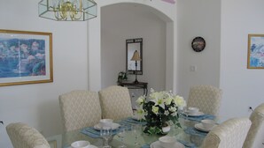 Un coin repas avec une table en verre, des chaises blanches et un vase de fleurs.