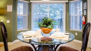 Uma área de refeições com mesa de vidro, cadeiras, um vaso de planta e um extintor na parede.