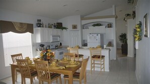 A dining area with a wooden table and chairs, a kitchen in the background, and a small island with a refrigerator. - Ov1584 - Glenbrook Resort - 4 Bed 3 Baths Villa (Clermont)