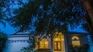 Una casa con garaje, una puerta principal y un árbol grande en el frente.