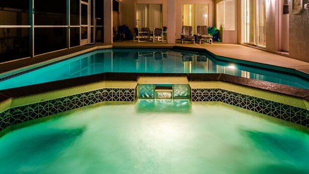Una piscina con borde de azulejos, un jacuzzi y una zona de estar con sillas y una mesa.