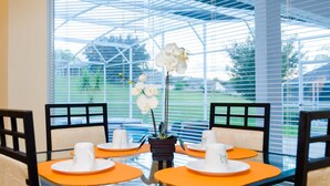 Un comedor con mesa y sillas de vidrio, una planta en maceta y vista a un paisaje verde a través de amplios ventanales.