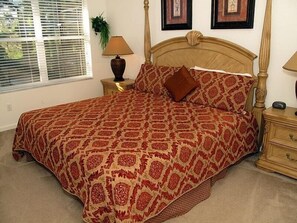 Quarto com uma cama grande, mesa de cabeceira com abajur e janela com persianas.