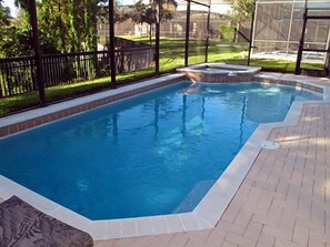 Uma piscina retangular com hidromassagem, rodeada por um deck de tijolos e uma cerca preta.