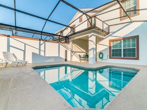 Ein Schwimmbecken mit geometrischer Glaskonstruktion, eine überdachte Terrasse und ein zweistöckiges Gebäude mit Balkon.