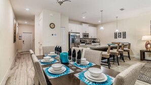 A dining area with a long table set for six, a kitchen in the background, and a chandelier above. - Ov2069 - Paradise Palms - 2 Bed 1 Baths Villa (Kissimmee)