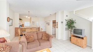 A living room with a sofa, a television on a wooden stand, and a dining area with a table and chairs.