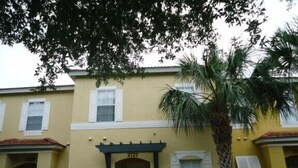 A yellow building with a number 2727, a small porch, and a palm tree.